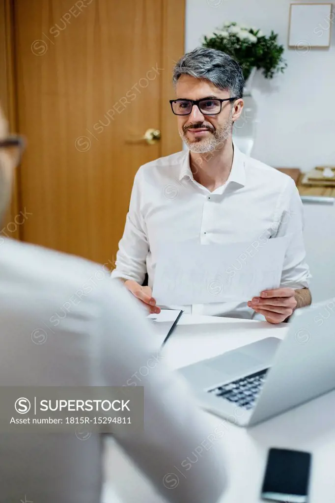 Smiling man at desk holding paper looking at colleague