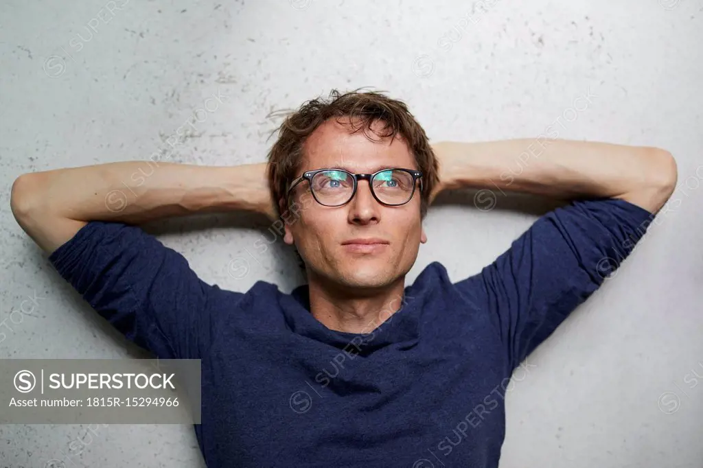 Portrait of man with hands behind head wearing glasses