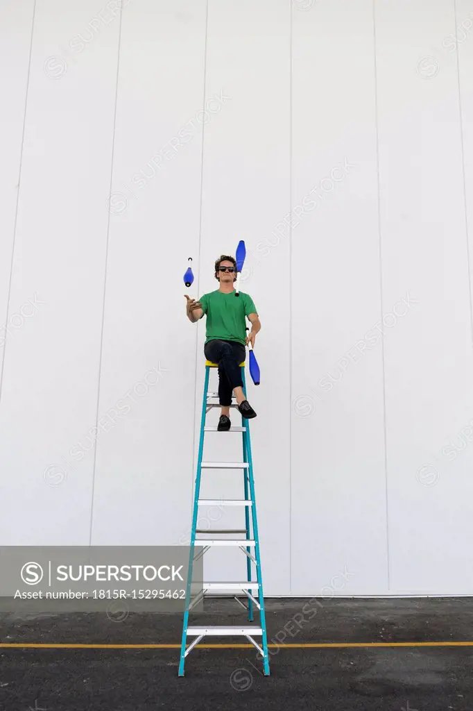 Acrobat wearing sunglasses, sitting on ladder, juggling