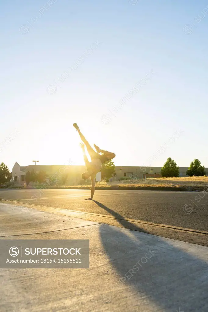 Acrobat practicing one-armed handstand on a road at sunset