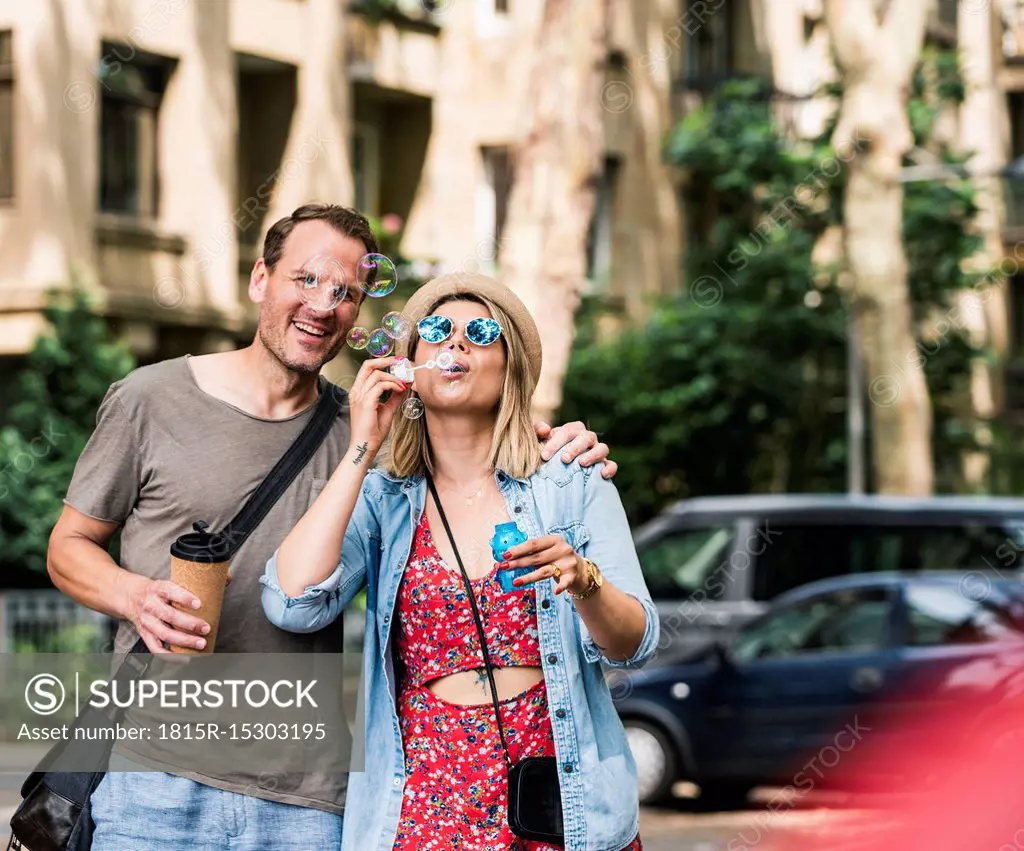 Happy couple with coffee to go blowing soap bubbles in the city