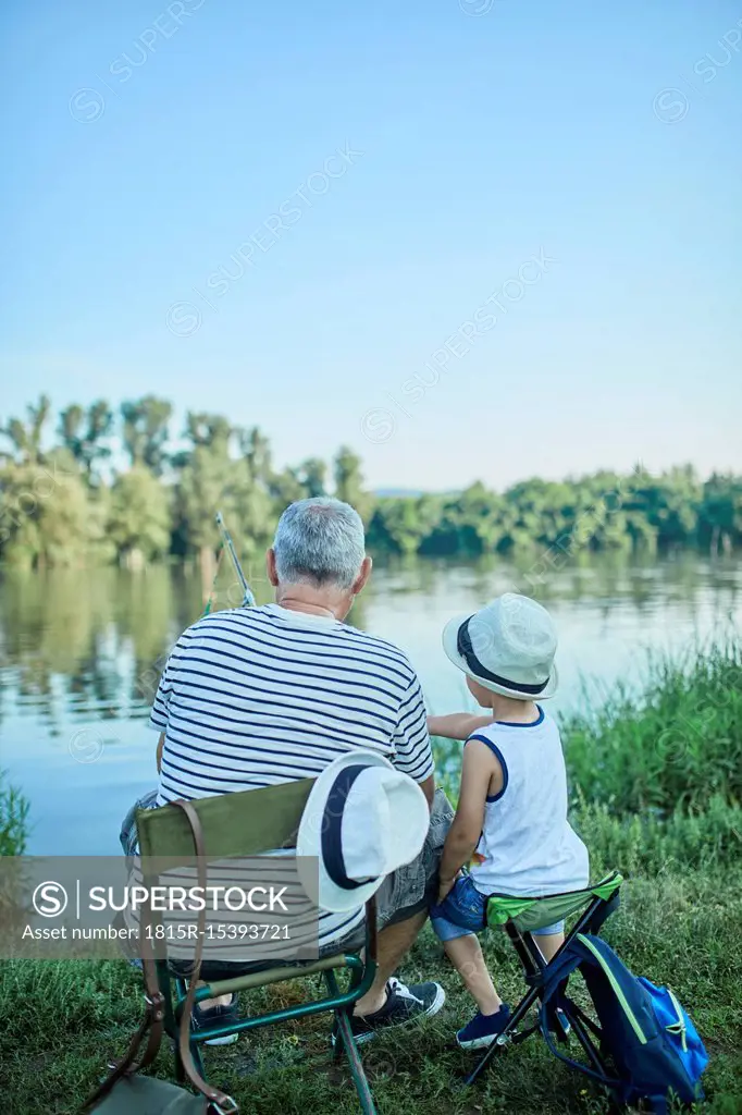 Back view of grandfather and grandson fishing togetehr at lakeshore