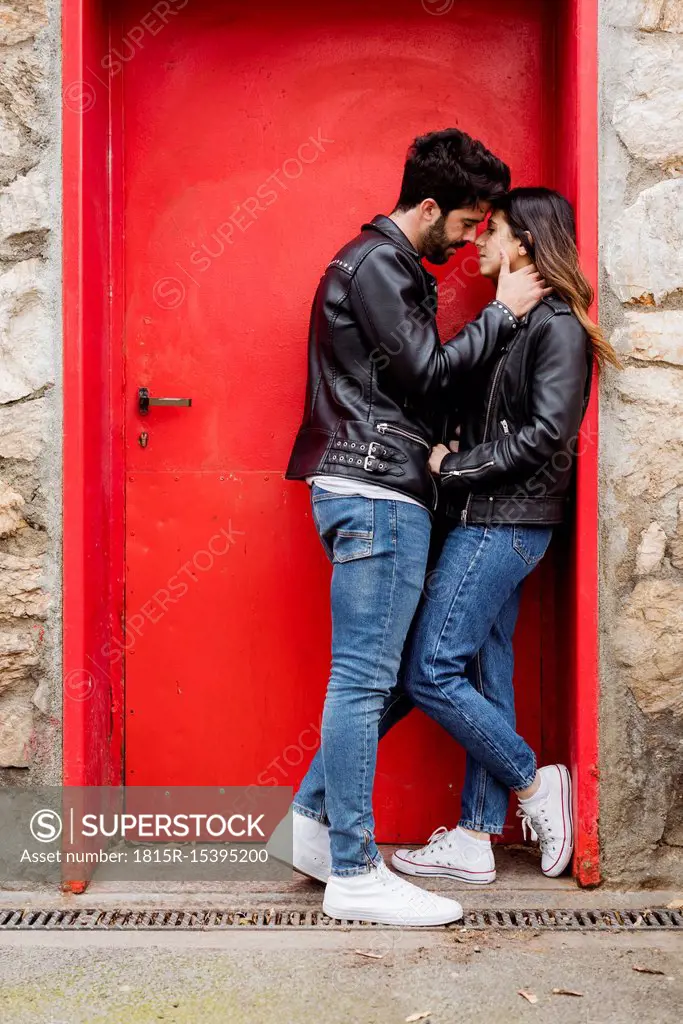 Affectionate young couple kissing at red door