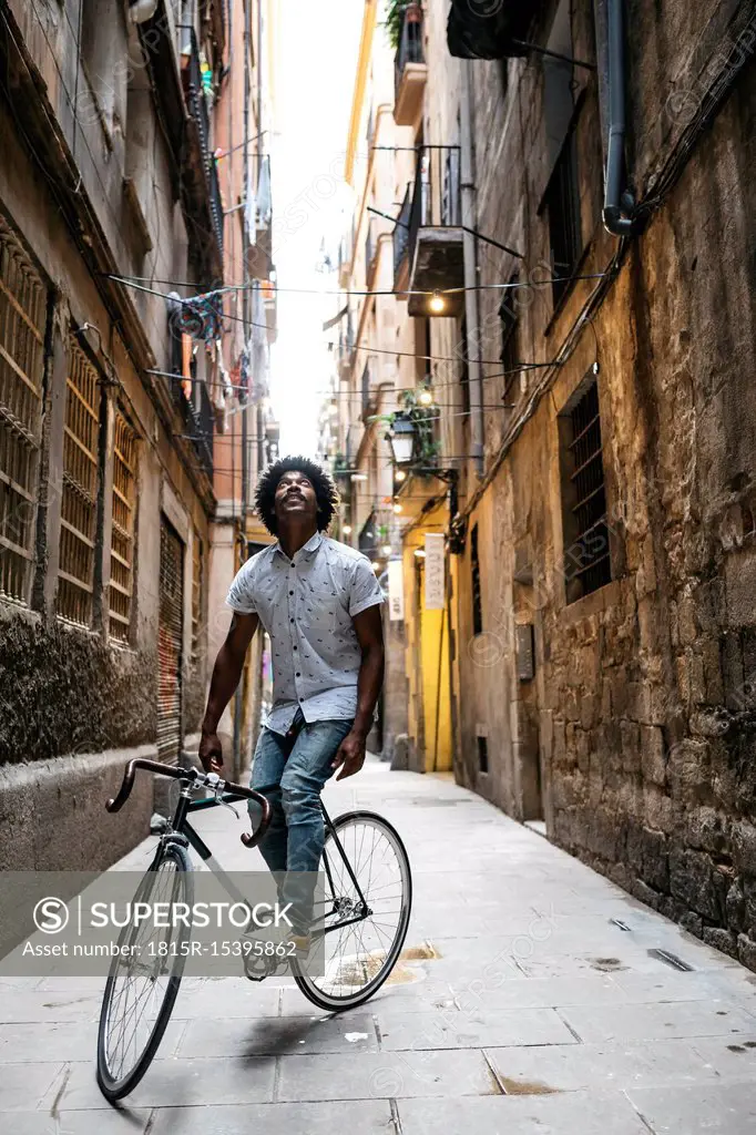 Spain, Barcelona, man standing with racing cycle in an alley looking up