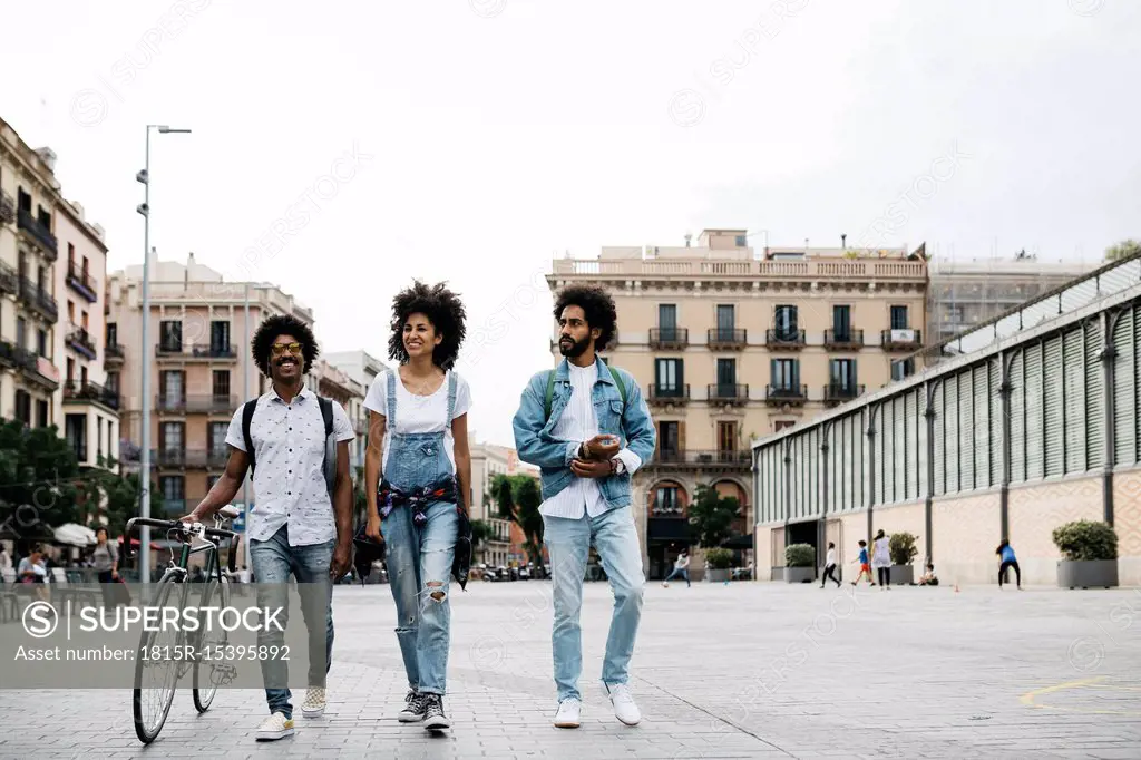 Spain, Barcelona, three friends with racing cycle crossing a square