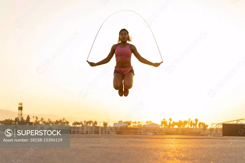 Spain, Barcelona, young black woman skipping rope at sunrise