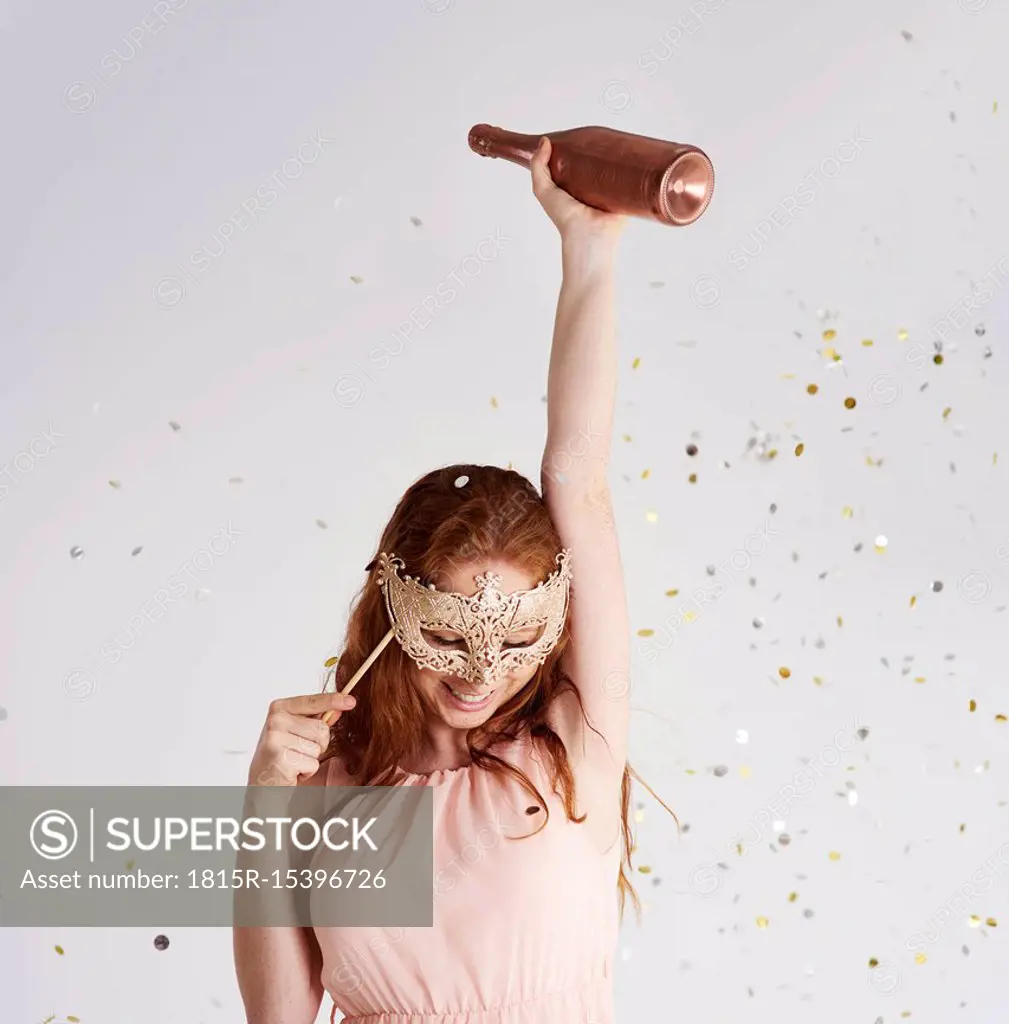 Happy young woman with bottle of champagne and masquerade mask