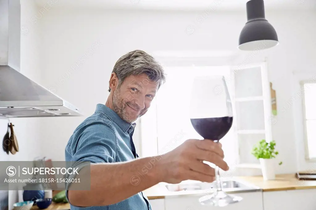 Man in kitchen toasting with glass of red wine