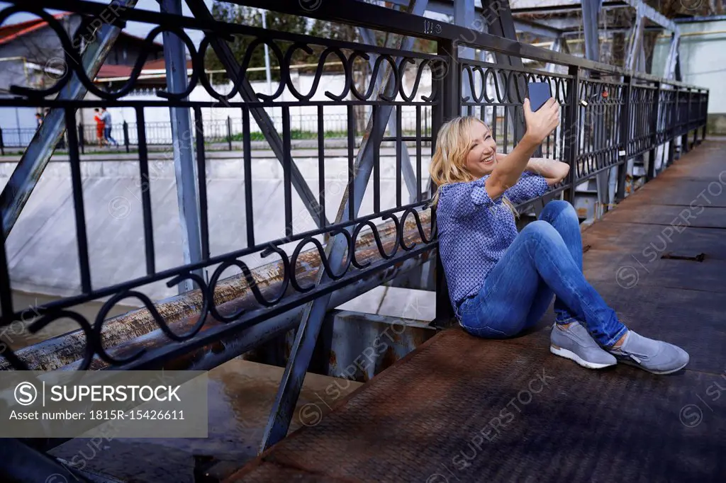 Blond woman sitting on bridge, taking selfie