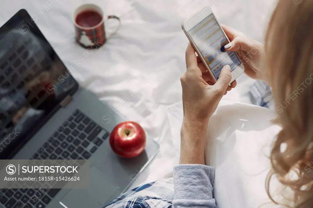 Woman sitting on bed with laptop, reading text messages