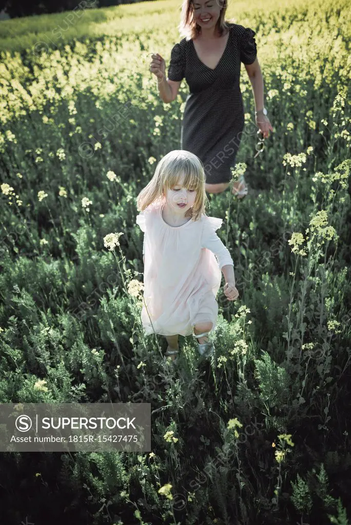 Portrait of little girl walking on rape field with her mother