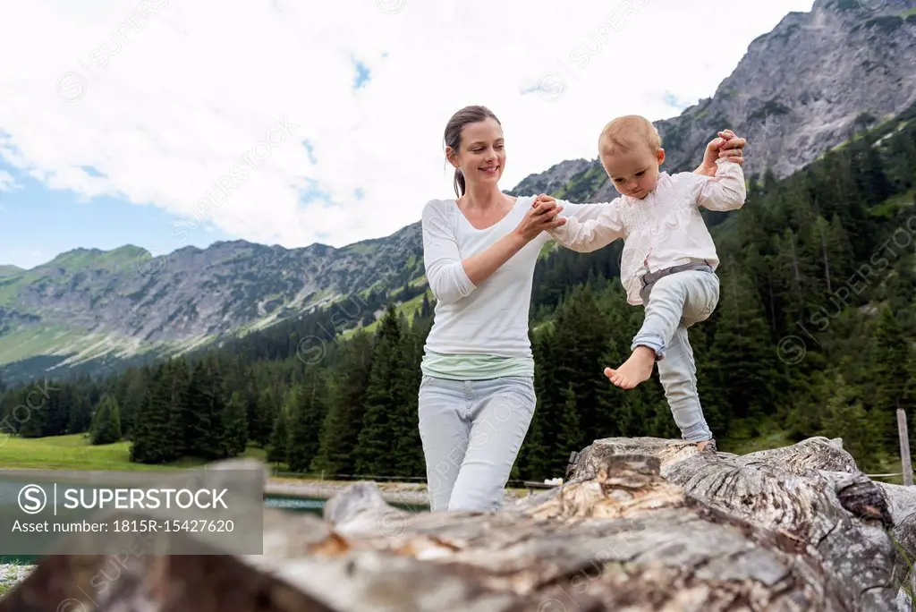 Germany, Bavaria, Oberstdorf, mother helping little daughter balancing on a log