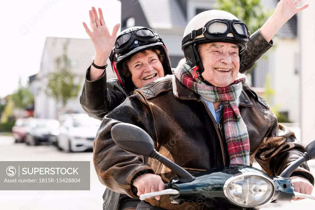 Happy senior couple having fun, riding motor scooter and waving