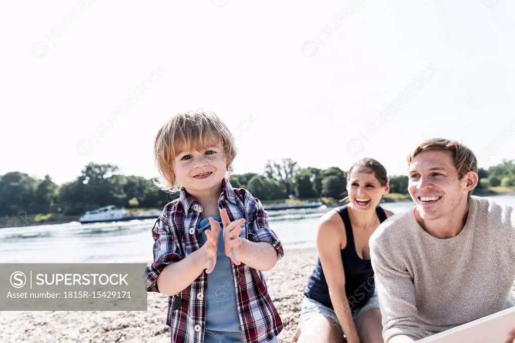 Happy boy clapping hands at the riverside with watching parents