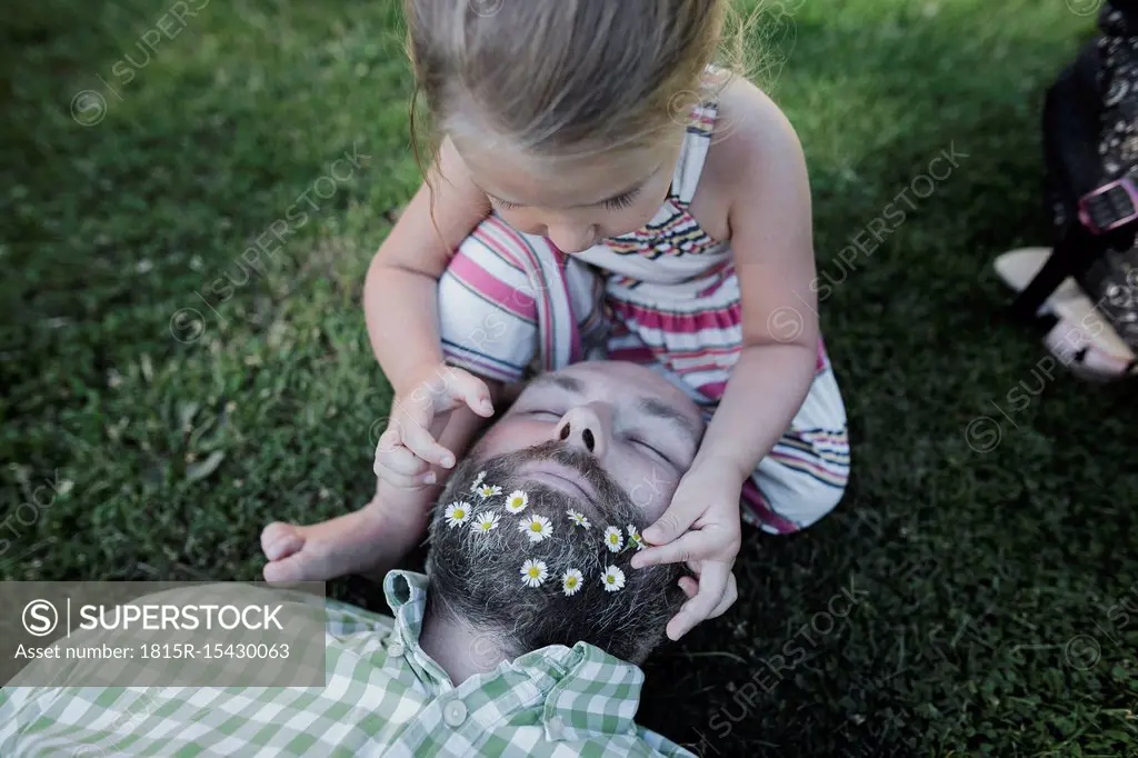 Little girl decorating father's beard with daisies on meadow in the garden