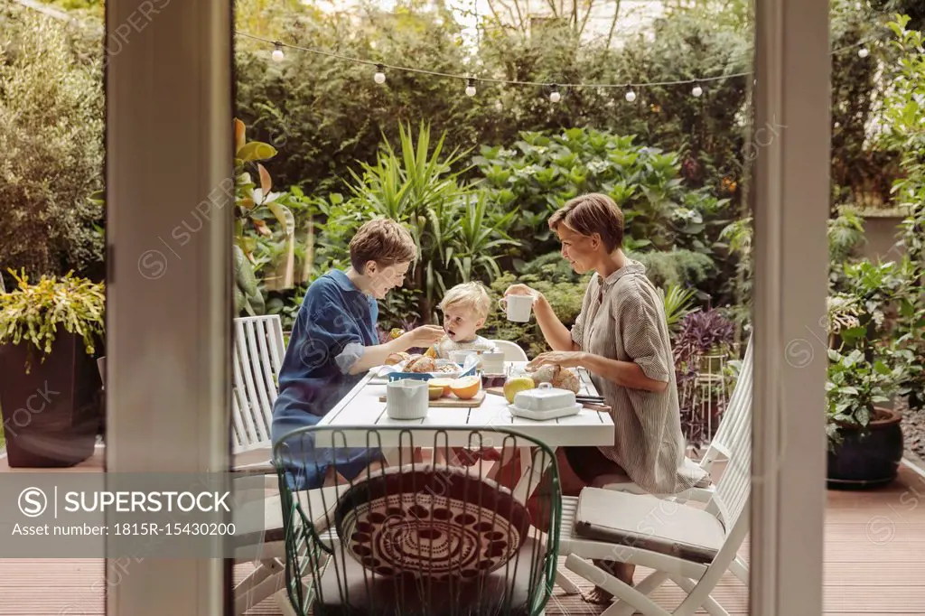 Two happy mothers at breakfast table outdoors with their child