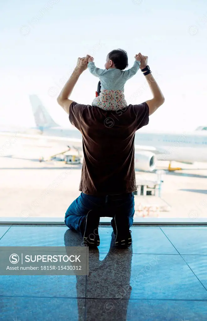 Man carrying a baby girl on his shoulders at the airport and looking at the airplanes, rear view