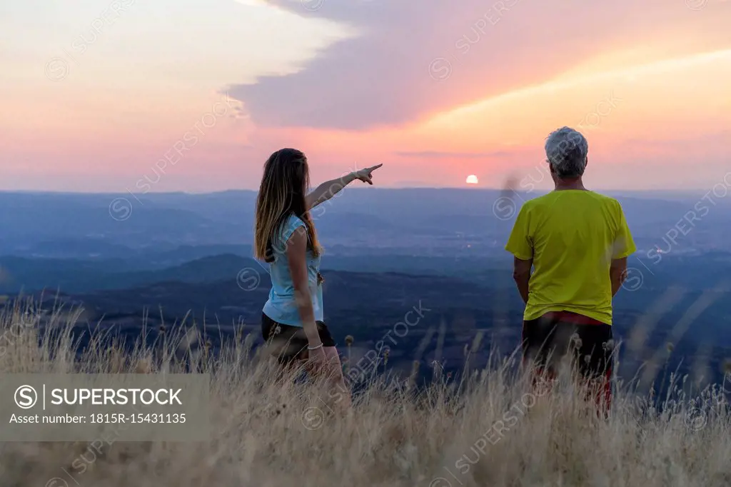 Spain, Catalonia, Montcau, senior father and adult daughter looking at view from top of hill during sunset