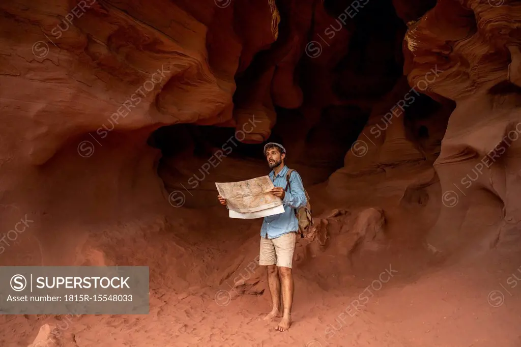 Young man standing in a cave, looking at map