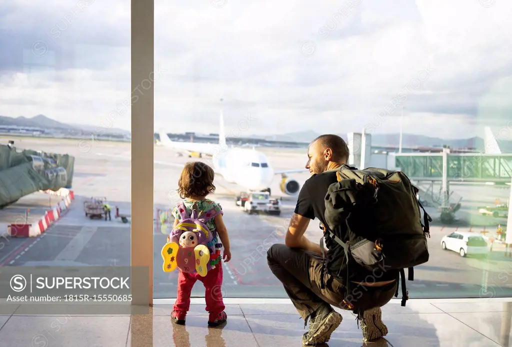 Father and daughter with backpacks at the airport looking at the planes