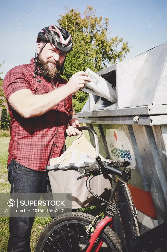 Portrait of cyclist recycling waste paper in paper bank