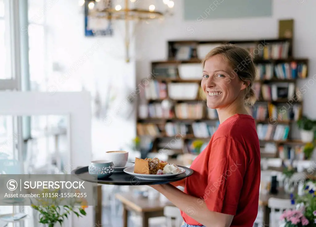 Portrait of smiling young woman serving coffee and cake in a cafe