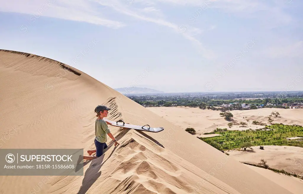 Peru, Ica, boy with sandboard on sand dune