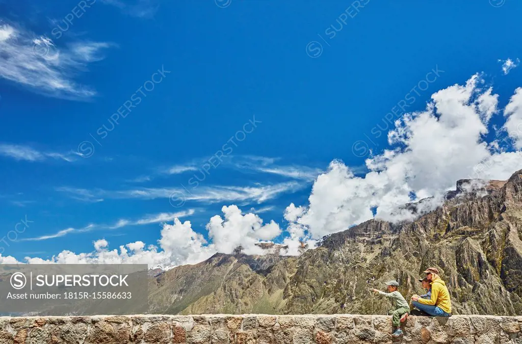 Peru, Chivay, Colca Canyon, woman sitting with sons on wall looking at canyon