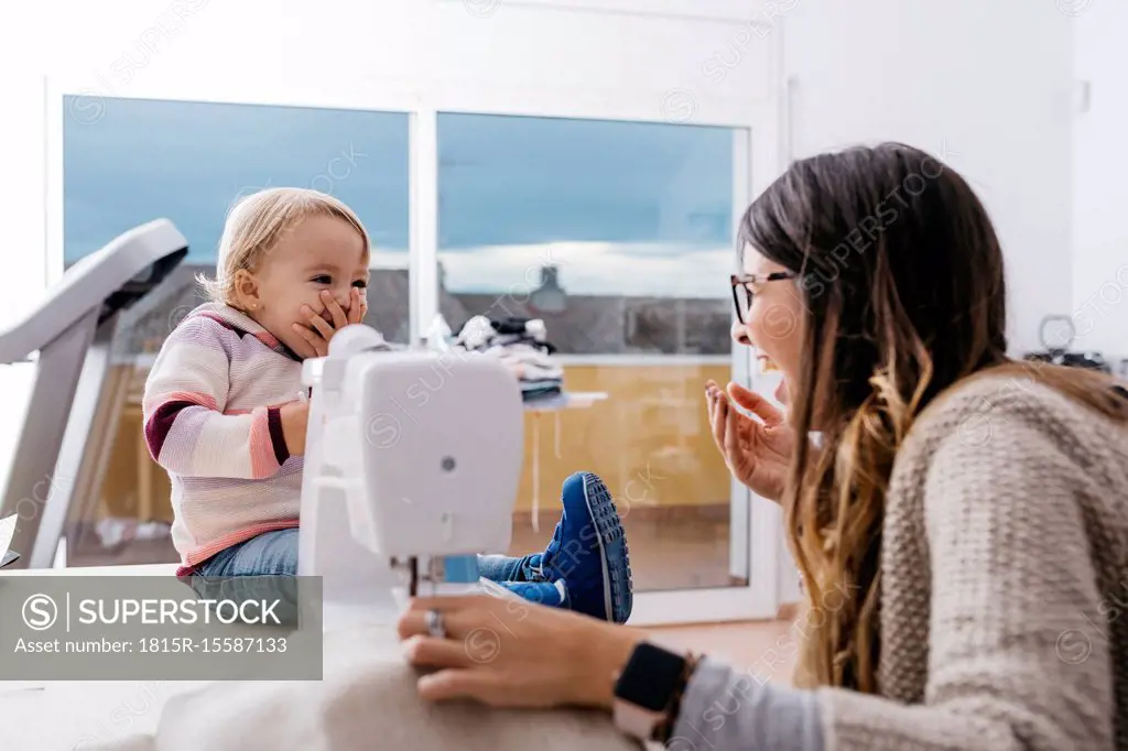 Happy mother with little daughter at home using sewing machine