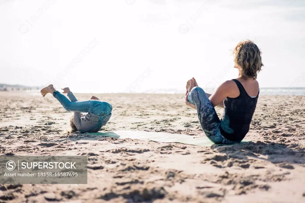 Mother and daughter practising yoga on the beach