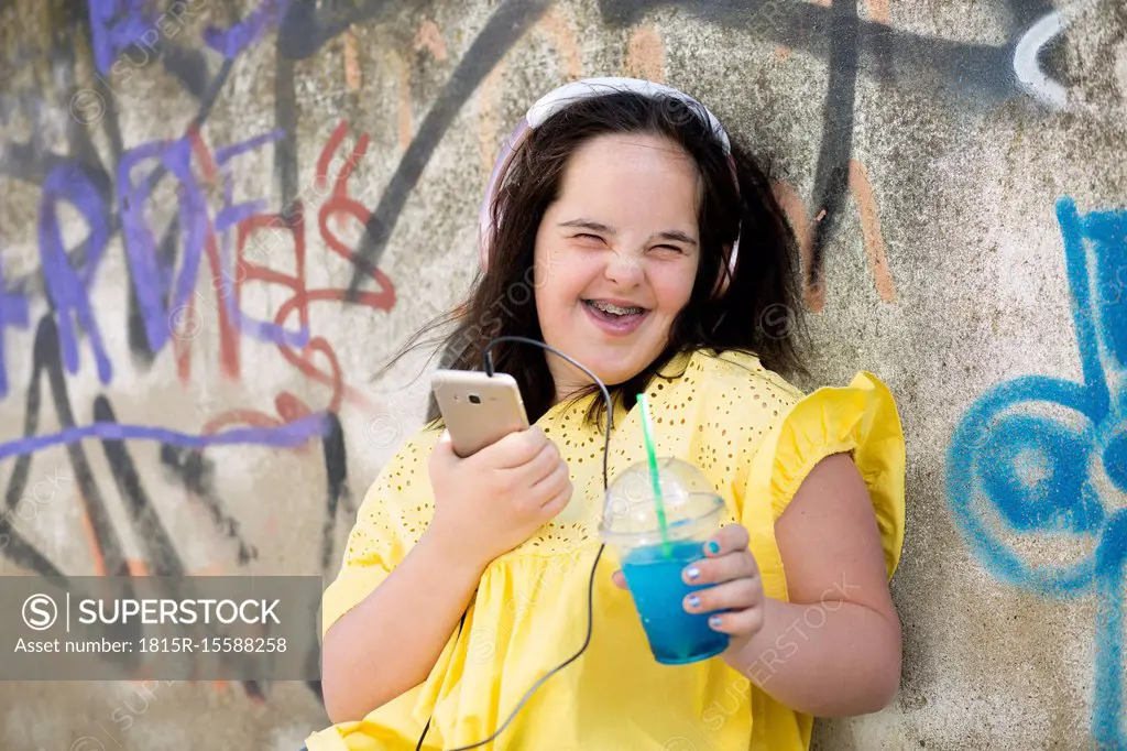 Teenager with down syndrome using smartphone, holding plastic cup