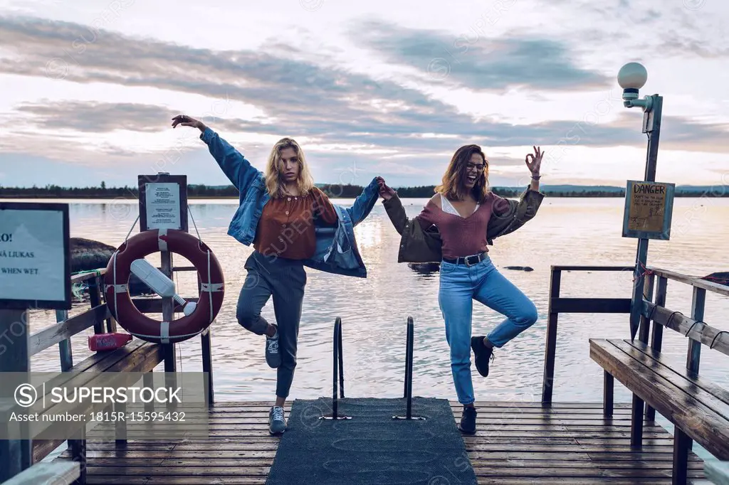 Two girl friends standing on one leg on a pier at Lake INari, Finland