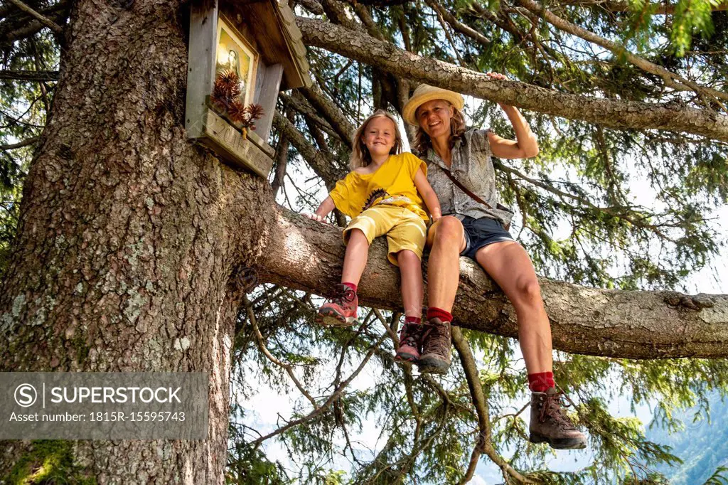 Portrait of smiling mother and daughter sitting in a tree