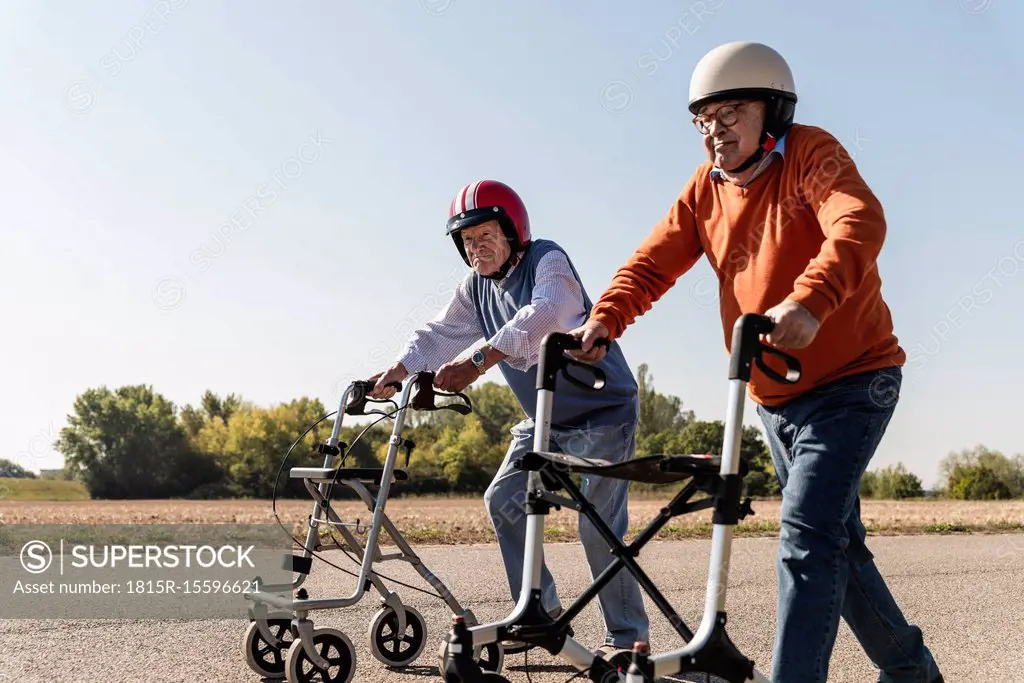 Two old friends wearing safety helmets, competing in a wheeled walker race