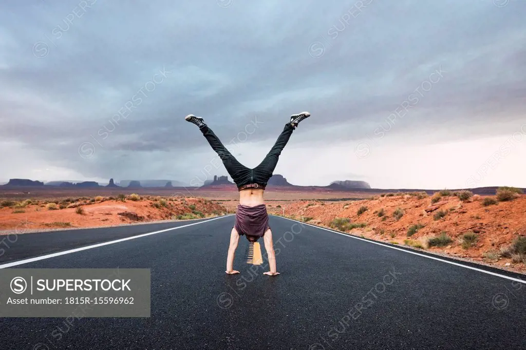 USA, Utah, Young man dong handstand on road to Monument Valley