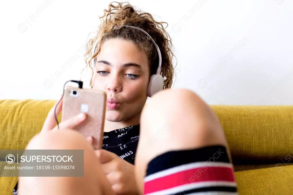 Portrait of whistling girl sitting on the couch listening music with headphones and smartphone