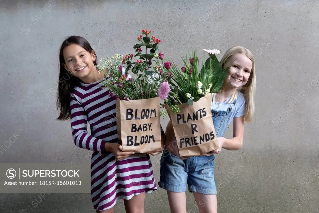 Portrait of two smiling girls holding paper bags with flowers