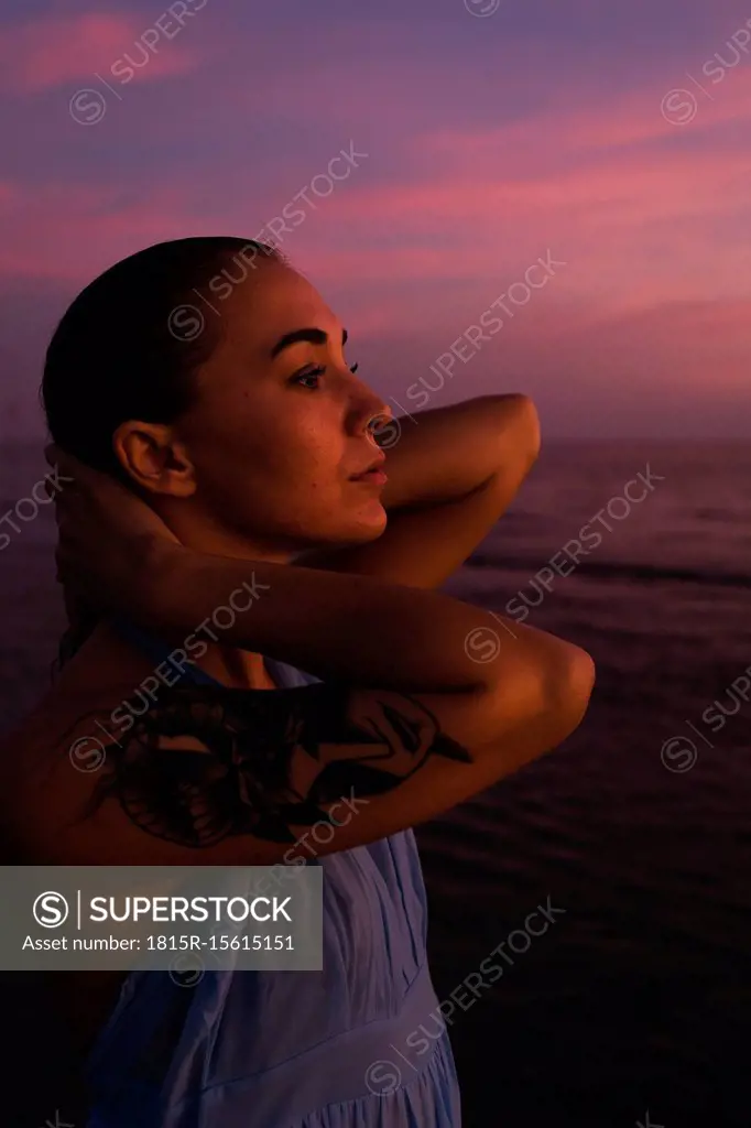 Profile of young woman with tattoo in front of the sea by sunset