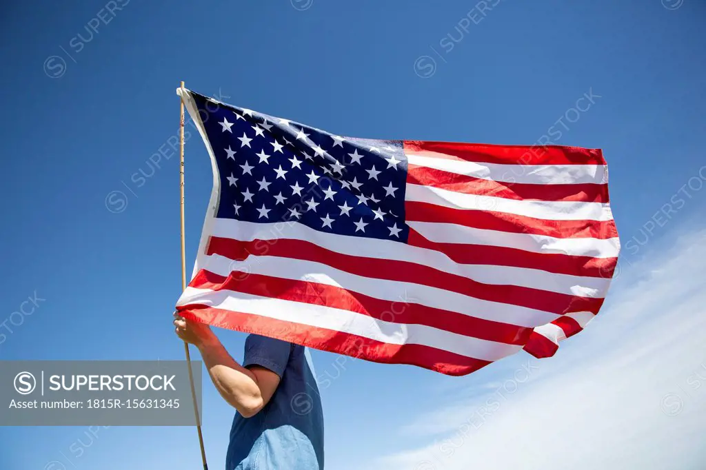 Man holding American flag under blue sky