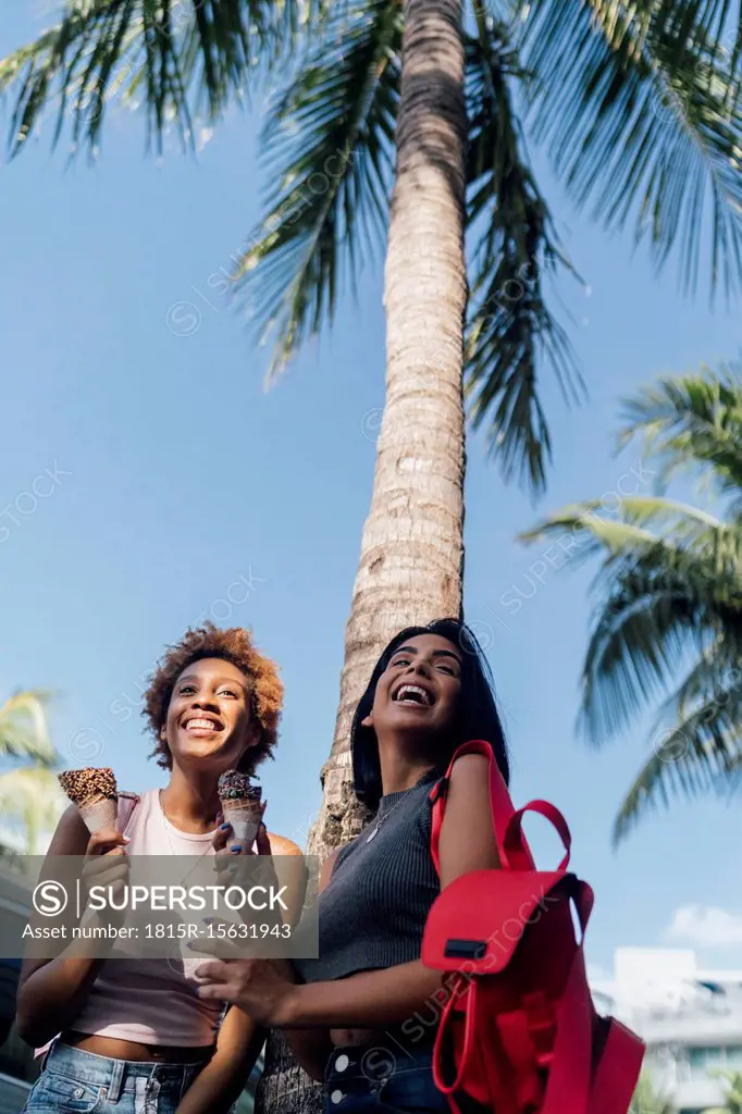 Two happy female friends with ice cream cones at a palm tree