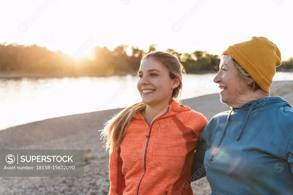 Fit grandmother and granddaughter walking at the river with arms around, having fun