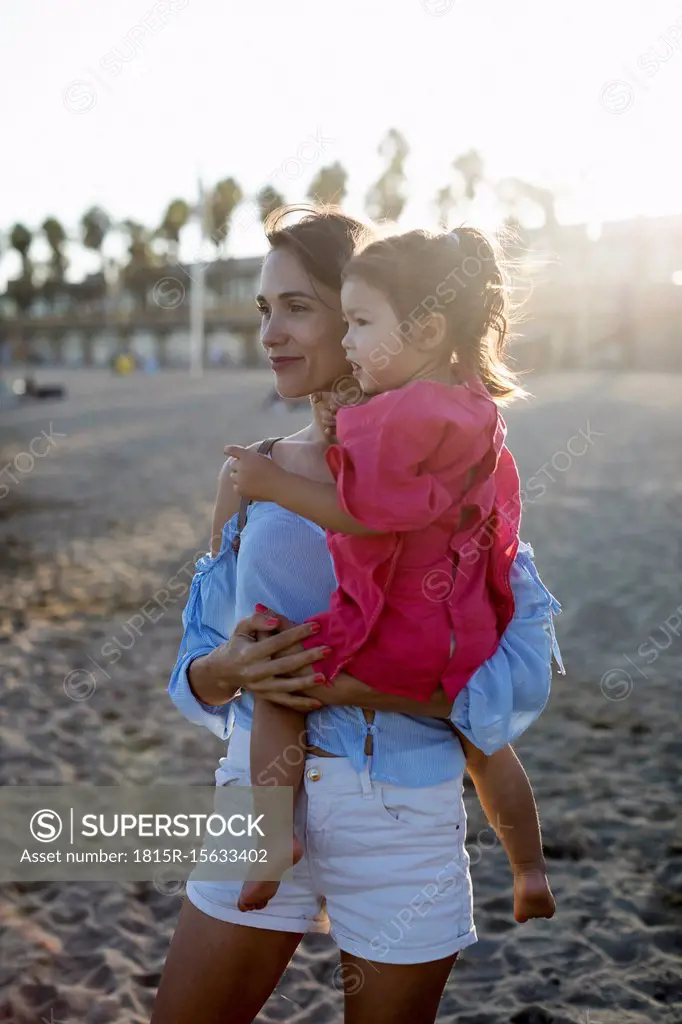 Mother and daughter standing on the beach at sunset