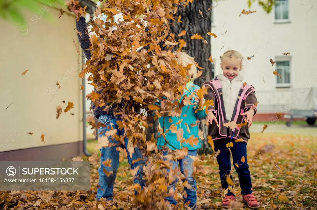 Three children throwing autumn leaves