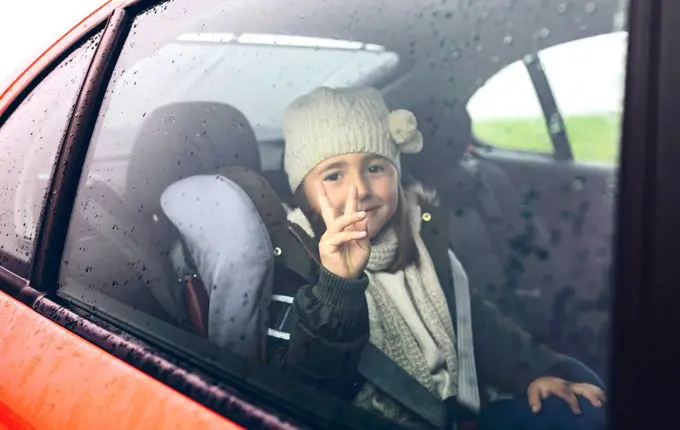 Portrait of happy little girl with wool cap doing victory sign while travelling in car