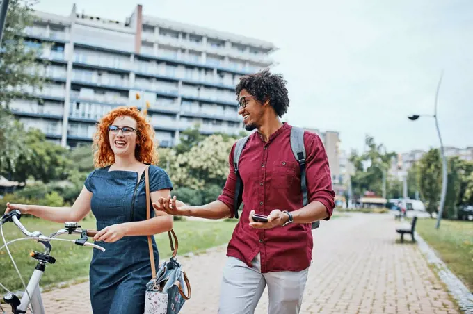 Friends walking in park, talking, woman pushing bicycle