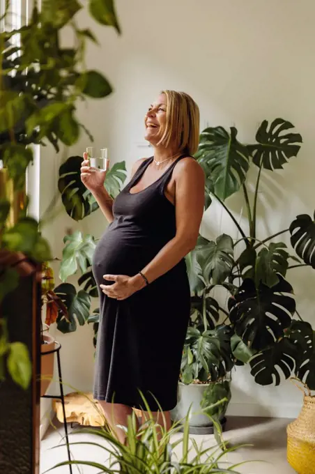 Happy mature pregnant woman having a glass of water at home
