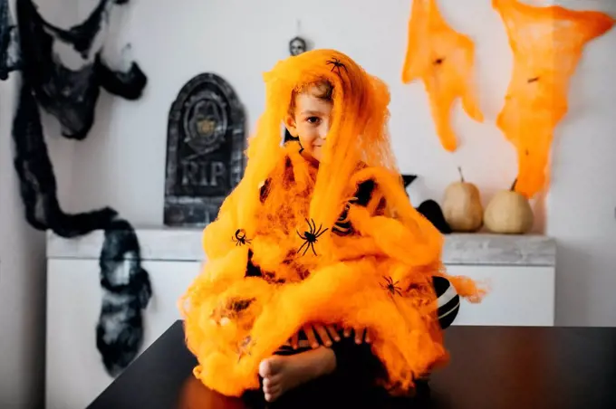 Little boy wrapped in orange spider web at Halloween