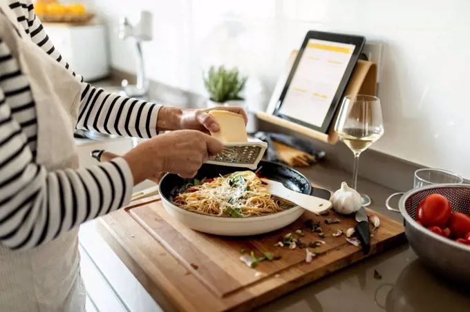 Close-up of woman with tablet cooking pasta dish in kitchen at home