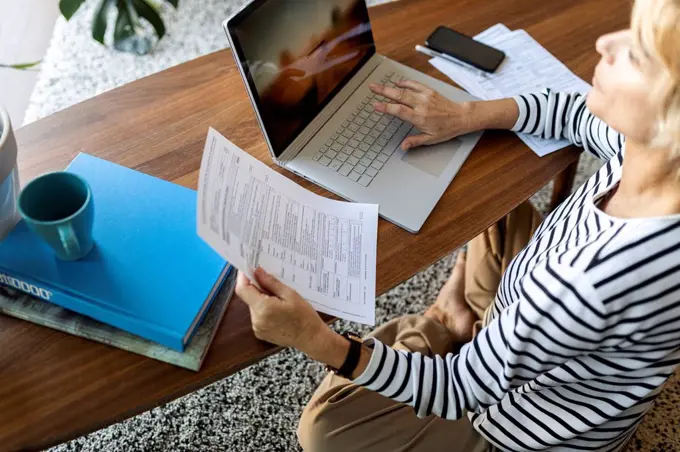 Mature woman with documents using laptop at home