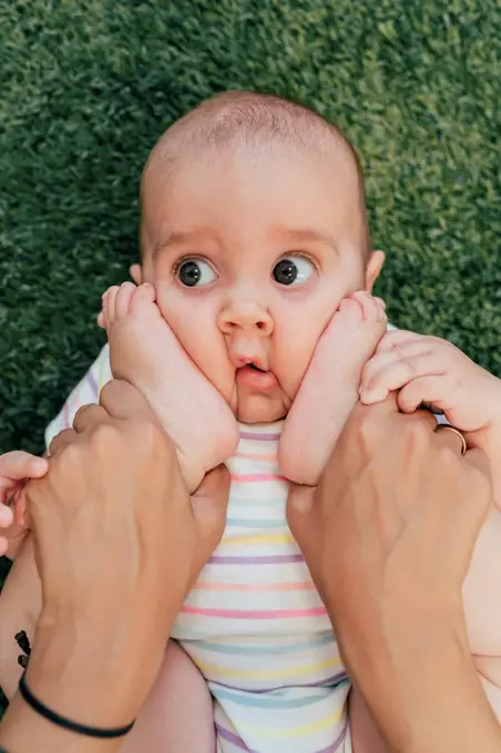 Young mother and baby exercising, girl looking sideways, feet in her face